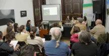 Personas reunidas escuchando una exposición y mirando una pantalla que refleja datos de la temática 